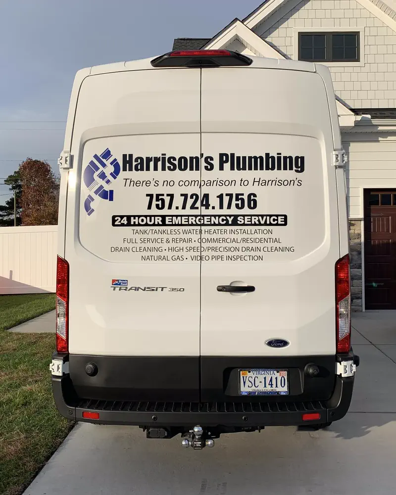 The back of Harrison's Plumbing's white Ford Transit van, lettered with the logo, the phone number 757.724.1756 and 24 hour emergency service, parked in a Virginia Beach driveway